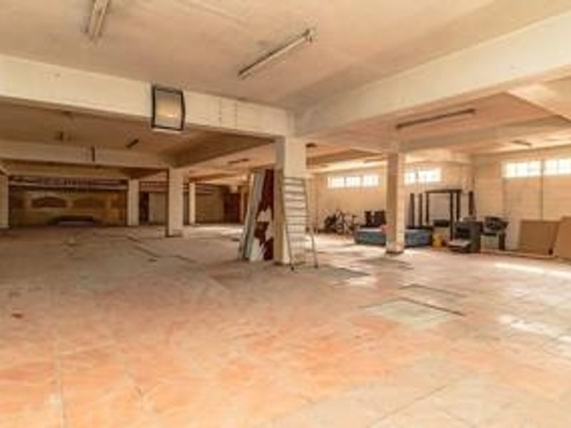 A large, open-plan commercial space featuring tiled flooring, exposed concrete ceilings, and structural support columns, suitable for various business or retail configurations.