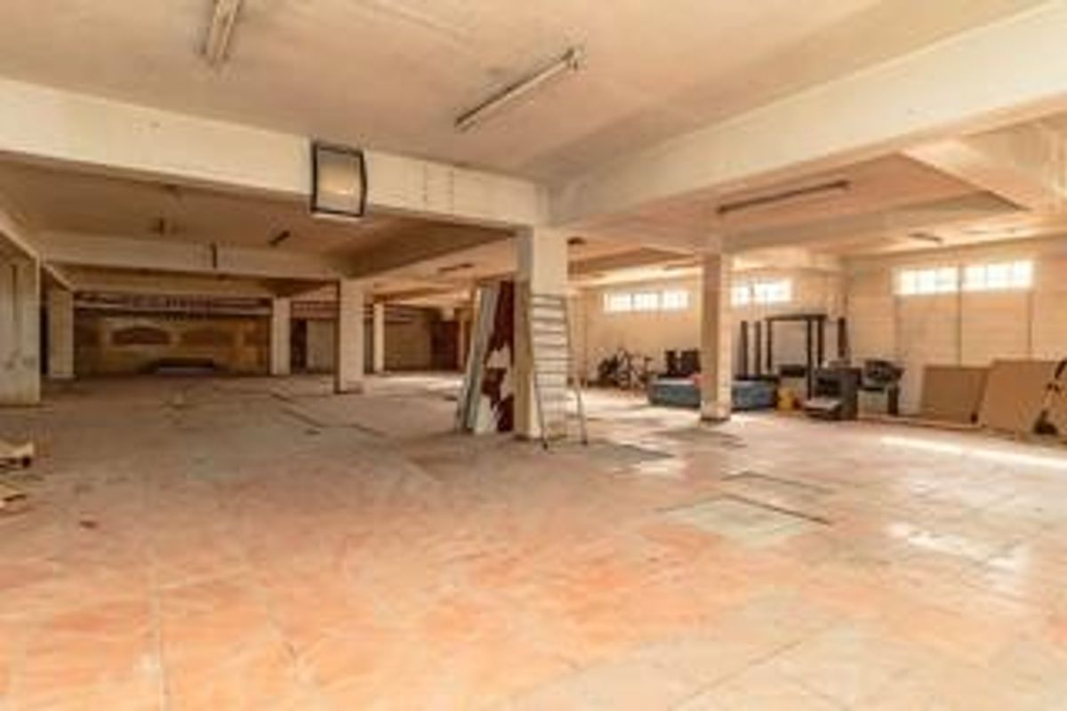 A large, open-plan commercial space featuring tiled flooring, exposed concrete ceilings, and structural support columns, suitable for various business or retail configurations.