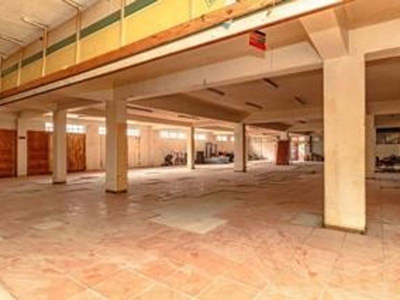 A large, open-plan commercial space featuring concrete columns, tiled flooring, and exposed structural beams, suitable for various business or retail configurations.