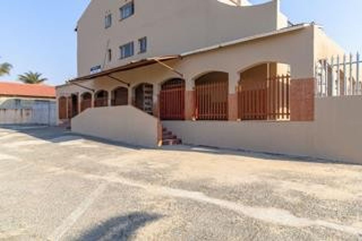 Front exterior view of a commercial building featuring a paved driveway, arched facade openings, and metal security fencing.