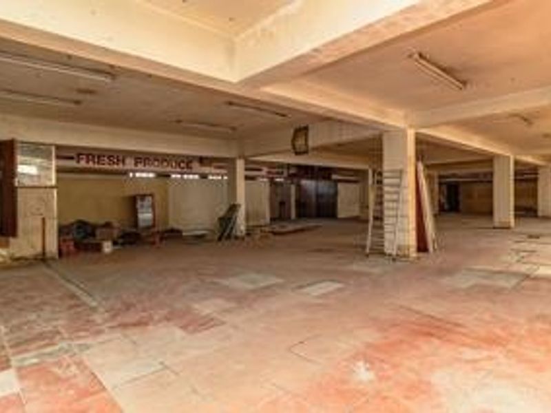 A large, vacant commercial open-plan space featuring concrete columns, tiled flooring, and industrial lighting, suitable for retail or warehouse conversion.