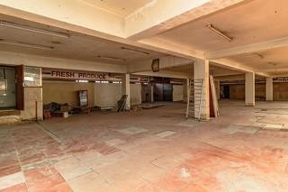 A large, vacant commercial open-plan space featuring concrete columns, tiled flooring, and industrial lighting, suitable for retail or warehouse conversion.