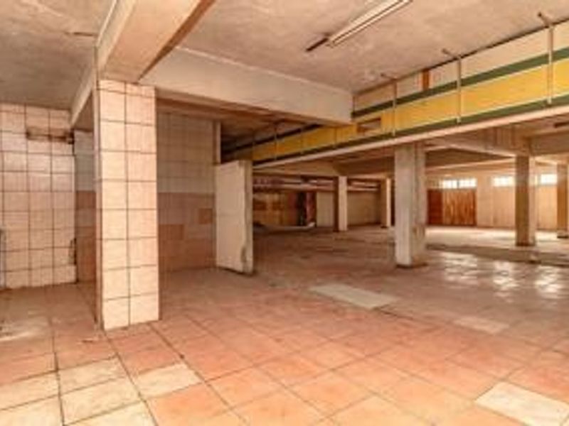 A large, vacant open-plan commercial space featuring tiled flooring, structural columns, and tiled wall finishes, requiring significant refurbishment.