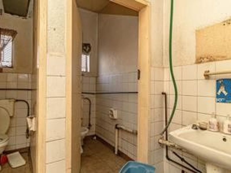 A dated commercial bathroom facility featuring basic ceramic tiling, wall-mounted washbasin, and toilet, requiring significant renovation and modernization of fixtures and finishes.