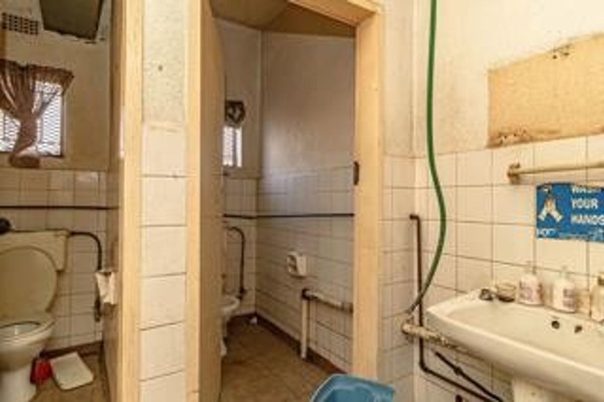 A dated commercial bathroom facility featuring basic ceramic tiling, wall-mounted washbasin, and toilet, requiring significant renovation and modernization of fixtures and finishes.