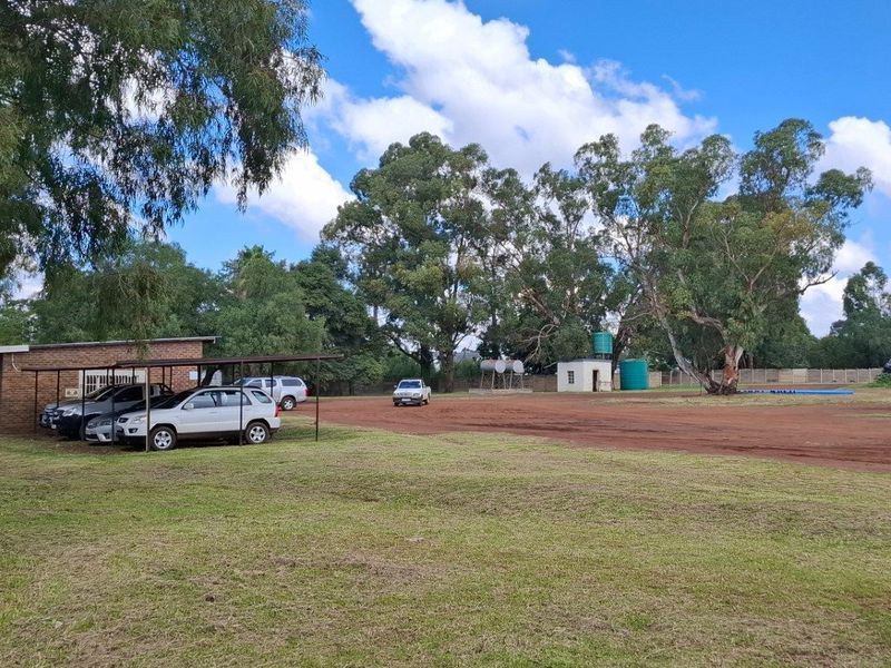 A wide view of a residential vacant land property featuring a brick building, carport, and water storage tanks on a large open plot.