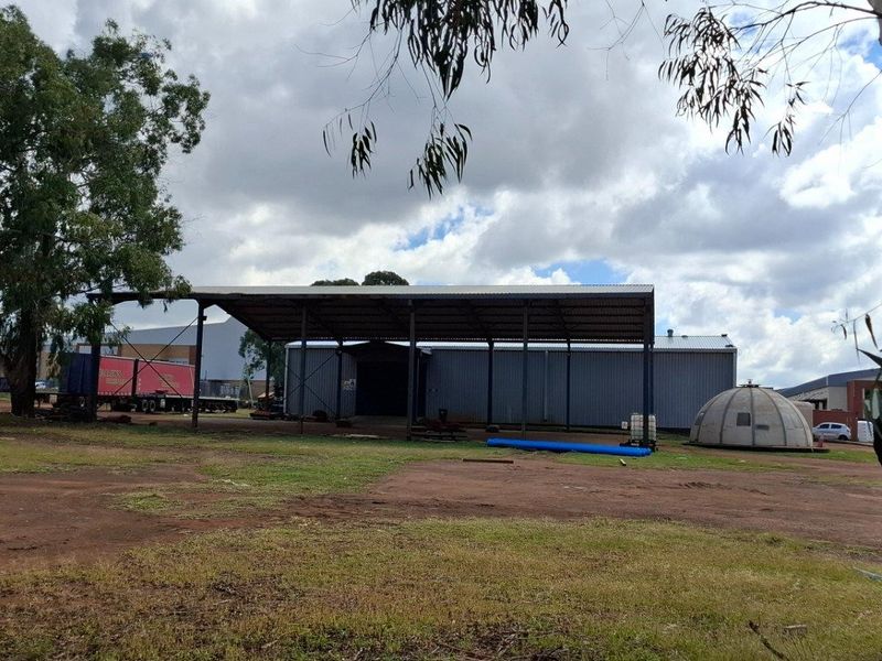 View of a large industrial metal shed structure with an open-sided canopy situated on a vacant residential plot.