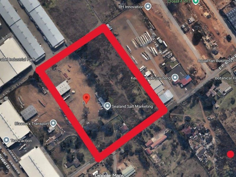 Aerial view of a vacant residential plot outlined in red, featuring open land and a small existing structure.