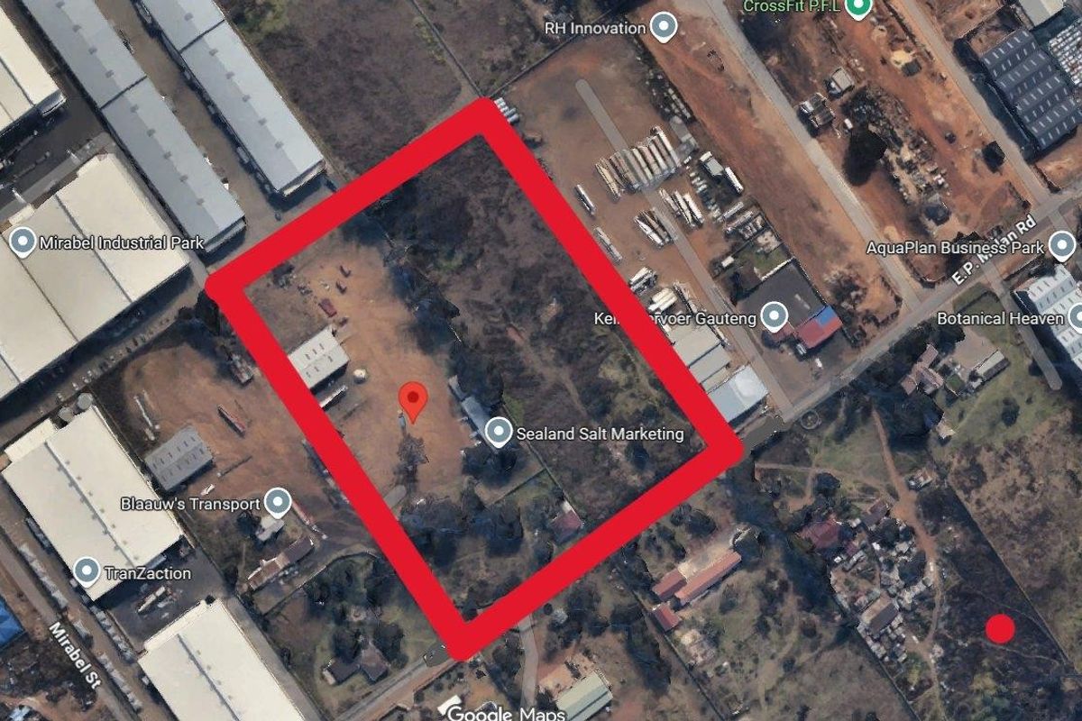 Aerial view of a vacant residential plot outlined in red, featuring open land and a small existing structure.