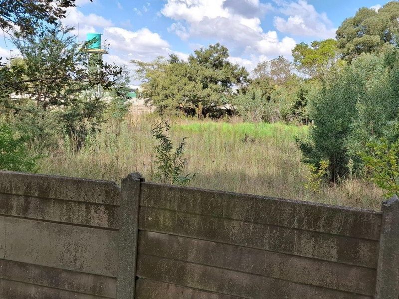 A view of a vacant residential plot featuring a precast concrete boundary wall and overgrown natural vegetation.