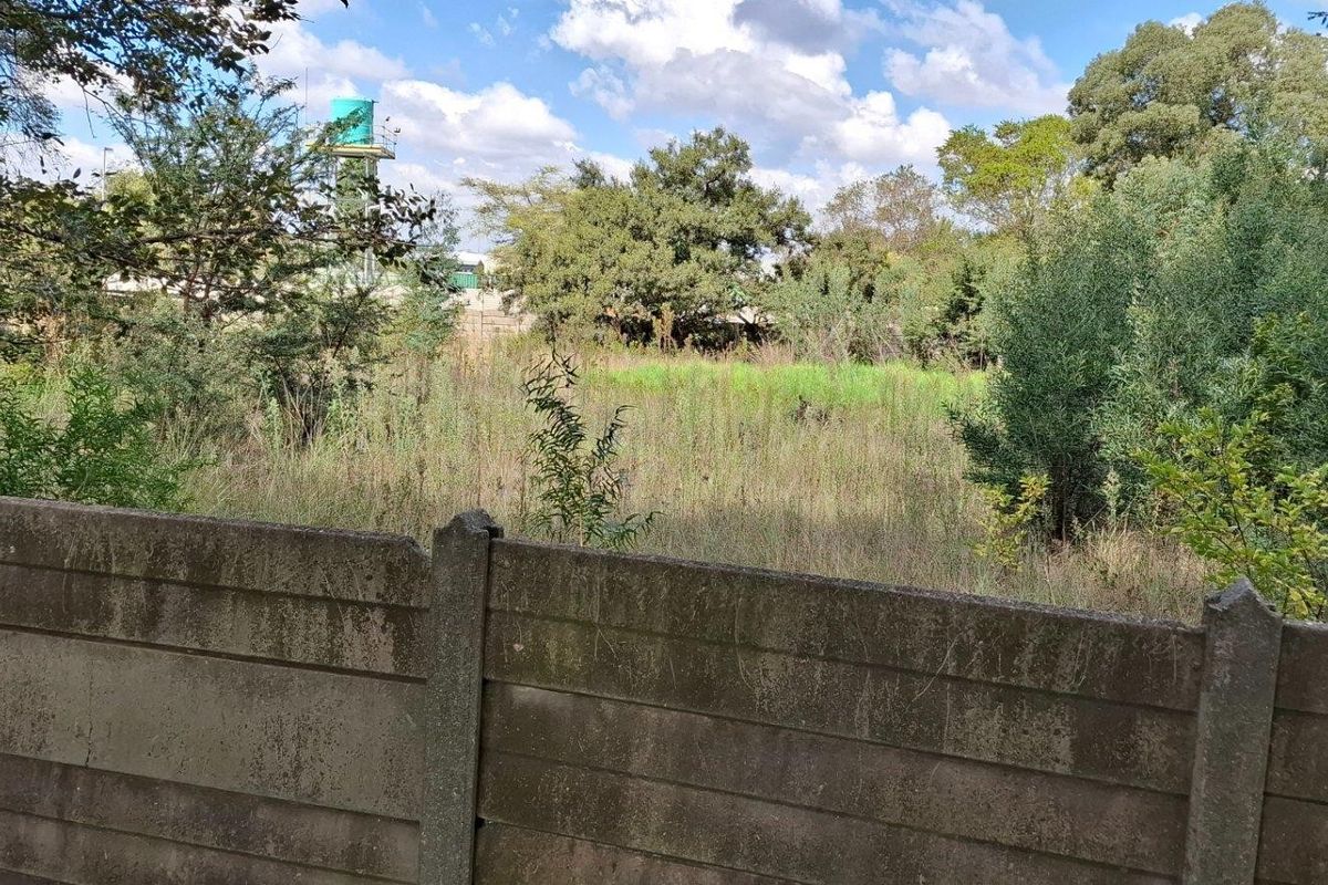 A view of a vacant residential plot featuring a precast concrete boundary wall and overgrown natural vegetation.
