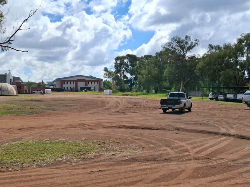 A wide-angle view of a large vacant residential or industrial plot featuring unpaved access areas and existing outbuildings.