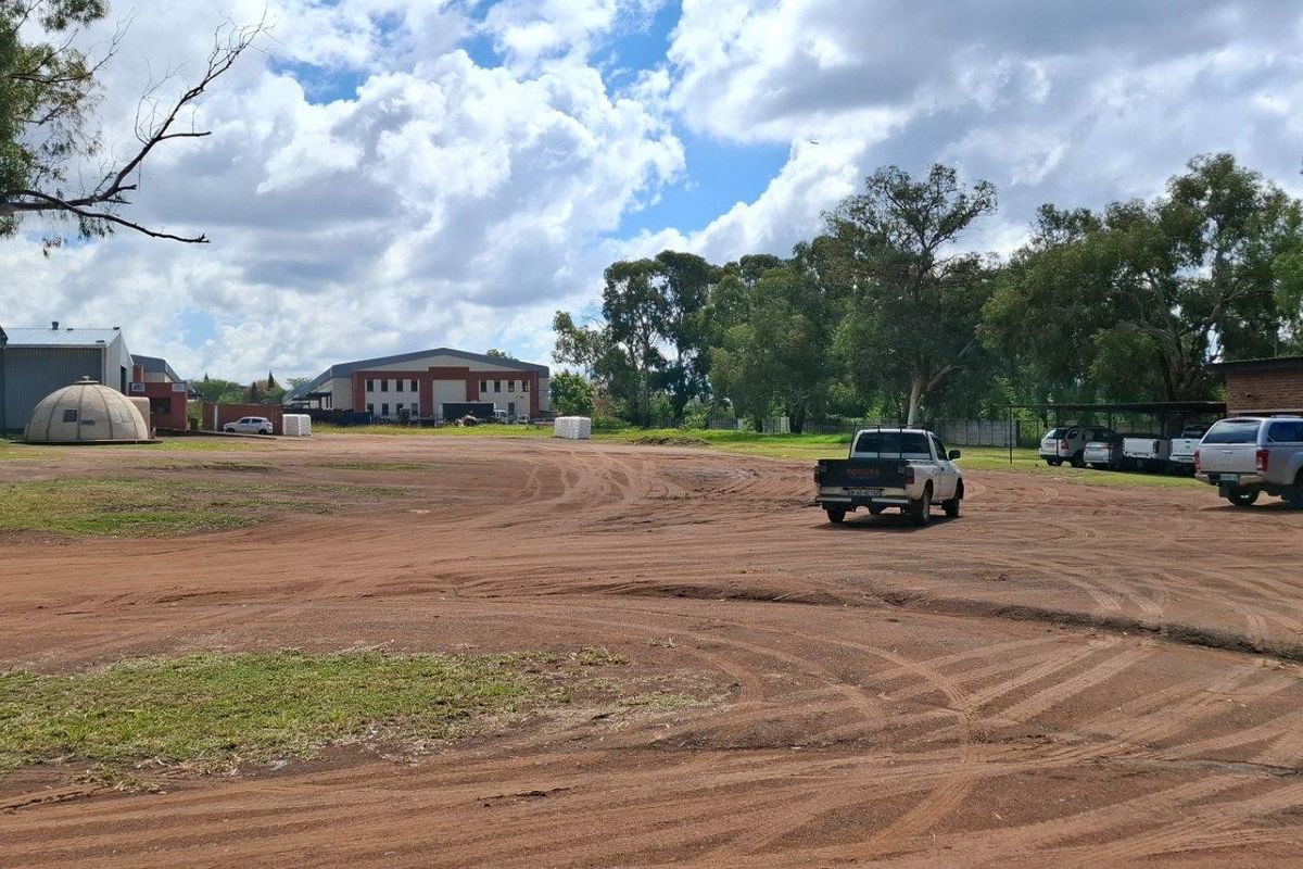 A wide-angle view of a large vacant residential or industrial plot featuring unpaved access areas and existing outbuildings.