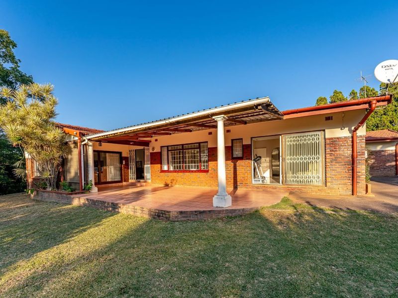 A spacious covered patio featuring tiled flooring, brick exterior walls, and sliding glass doors with security gates, overlooking the garden area.