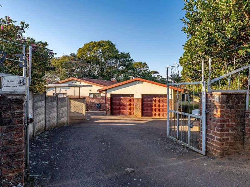 Front view of the property featuring a paved driveway, double garage with brick facade, and secure gated entrance with perimeter walling.