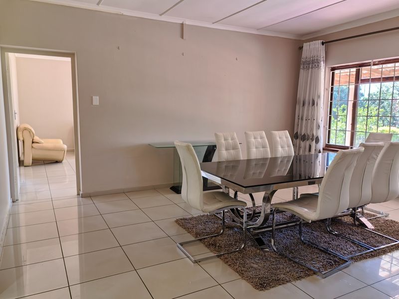 A bright dining room featuring neutral walls, large format floor tiles, and a window with security bars, offering a clean and functional space.