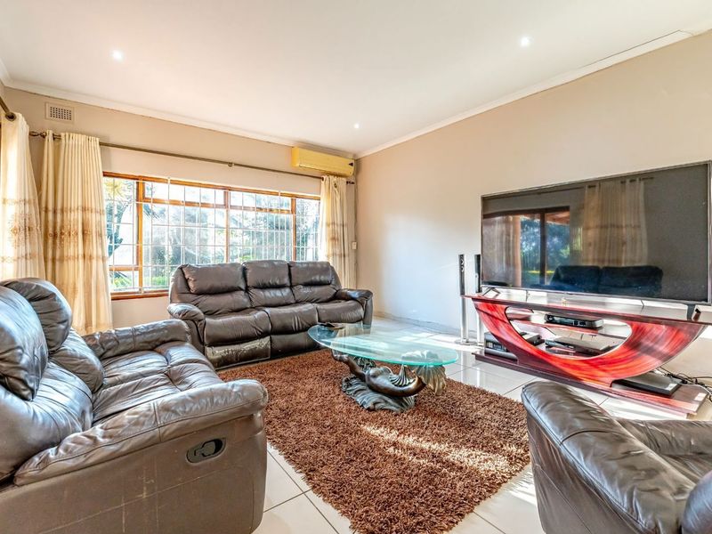 A comfortable living room featuring tiled flooring, recessed downlighting, and a wall-mounted split-system air conditioner, with large windows providing natural light.