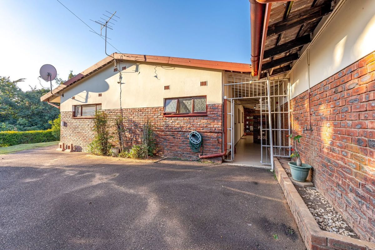 Rear exterior view of the property featuring a brick facade, asphalt driveway, and secure gated access point.
