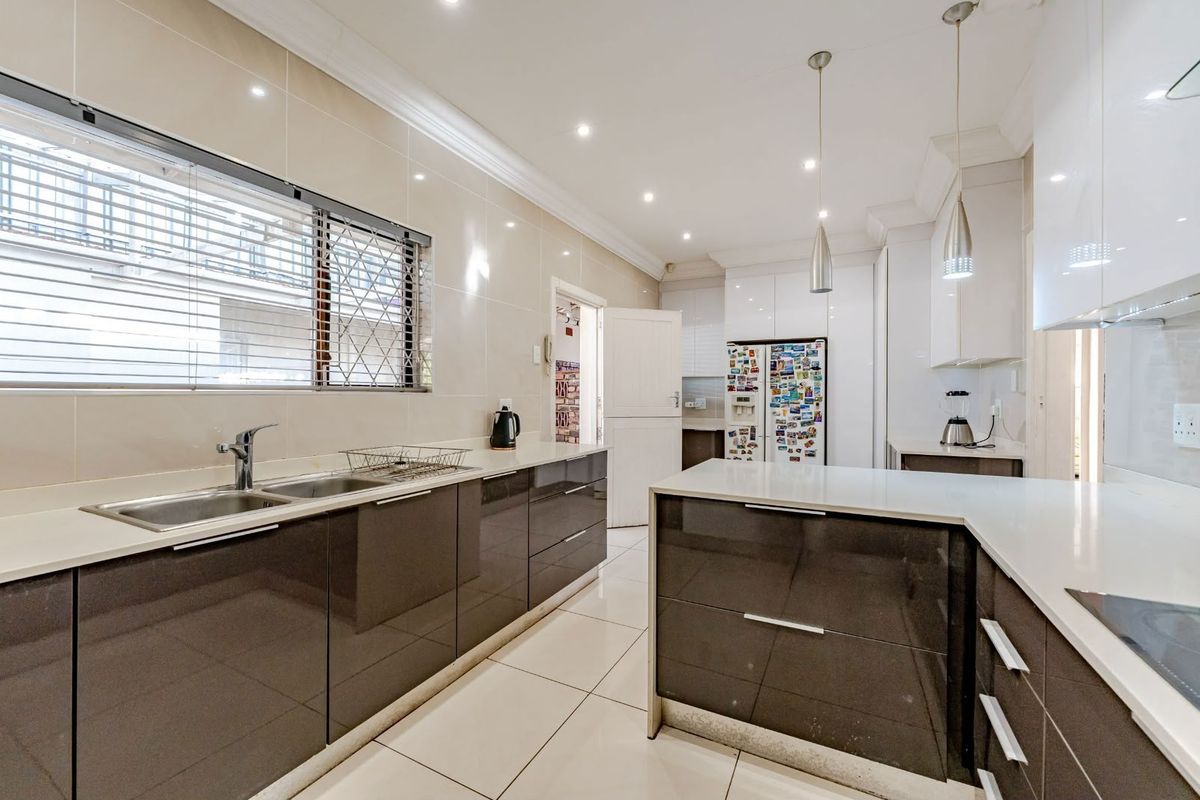 Modern kitchen featuring high-gloss cabinetry, stone countertops, a double basin sink, and sleek tiled finishes with integrated lighting.