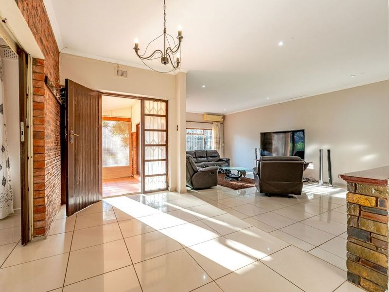 Spacious living area featuring polished tile flooring, an exposed brick feature wall, stone-clad pillar, and direct access to an outdoor patio area.