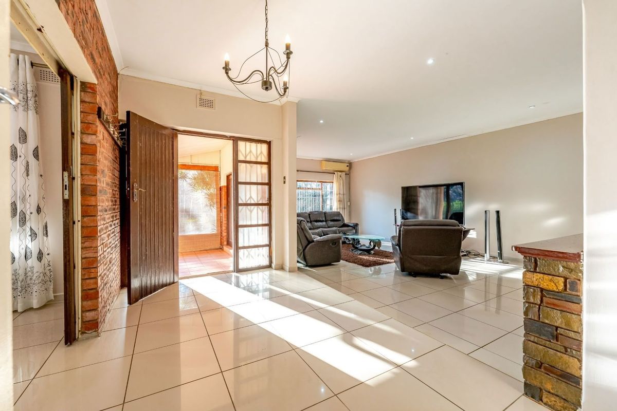 Spacious living area featuring polished tile flooring, an exposed brick feature wall, stone-clad pillar, and direct access to an outdoor patio area.