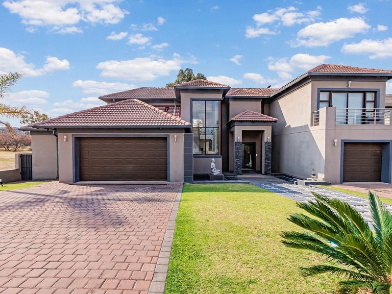 Modern double-story residential home featuring a paved driveway, double garage, stone-clad entrance, and a balcony, set on a well-maintained landscaped property.