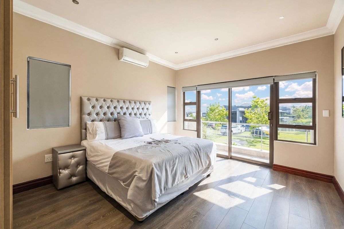 A well-lit bedroom featuring laminate flooring, recessed downlights, a split-system air conditioner, and sliding glass doors opening to a balcony.