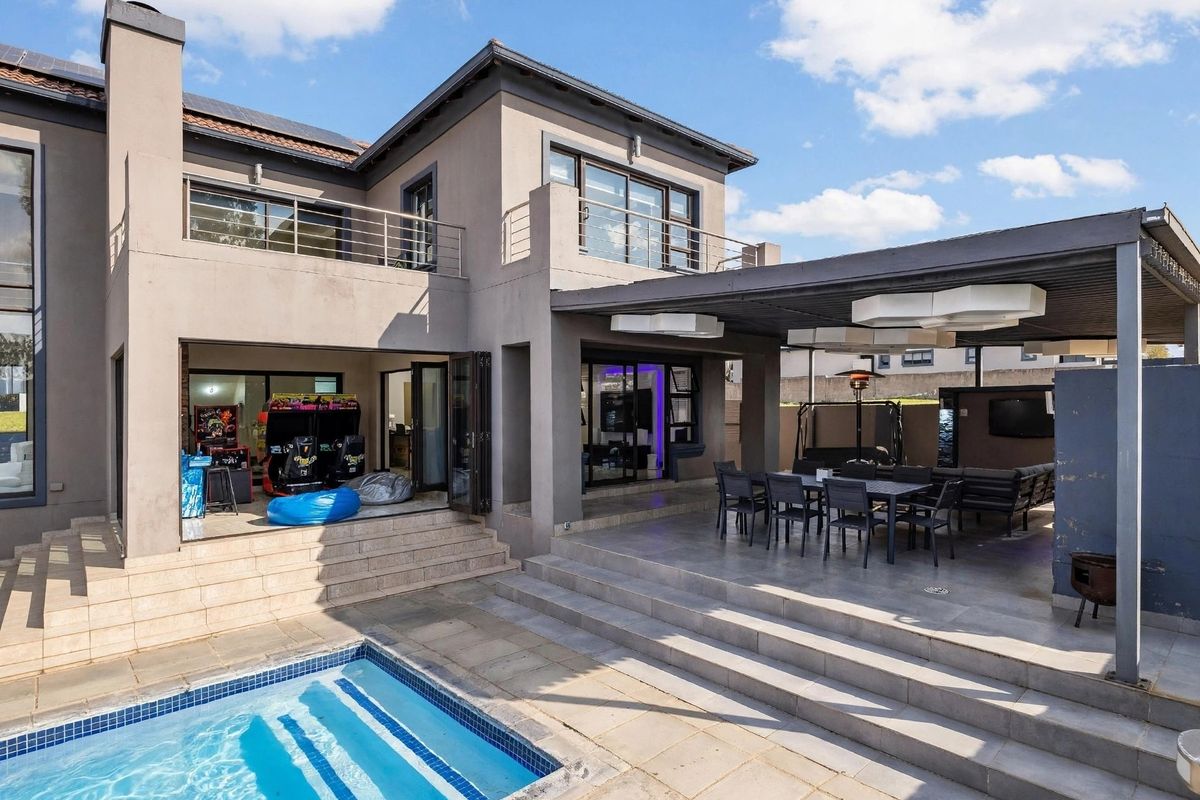 Rear exterior view featuring a covered patio, swimming pool, and upper-level balcony with modern architectural finishes and bi-fold doors.