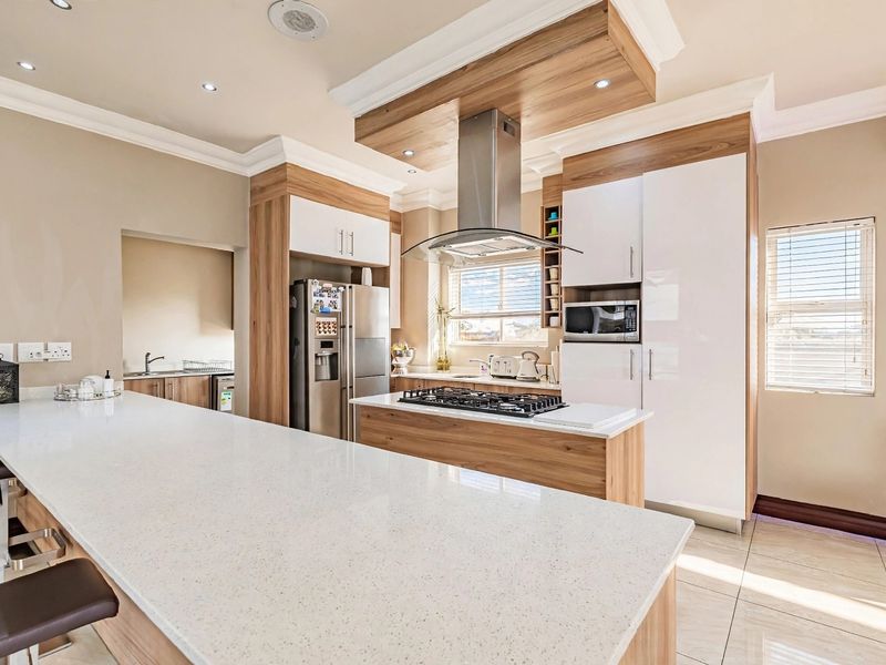 Modern kitchen featuring a large island with quartz countertops, gas hob, integrated appliances, and a separate scullery area with ample cabinetry.