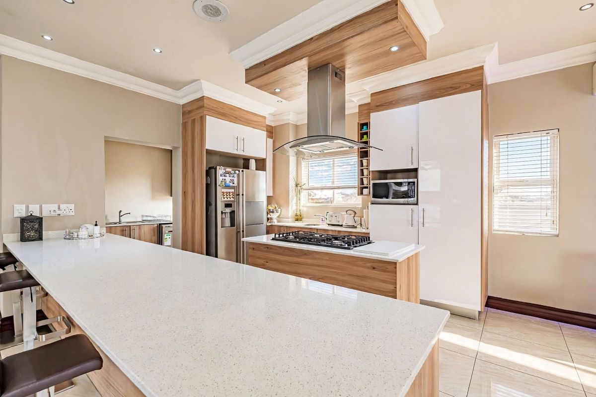 Modern kitchen featuring a large island with quartz countertops, gas hob, integrated appliances, and a separate scullery area with ample cabinetry.