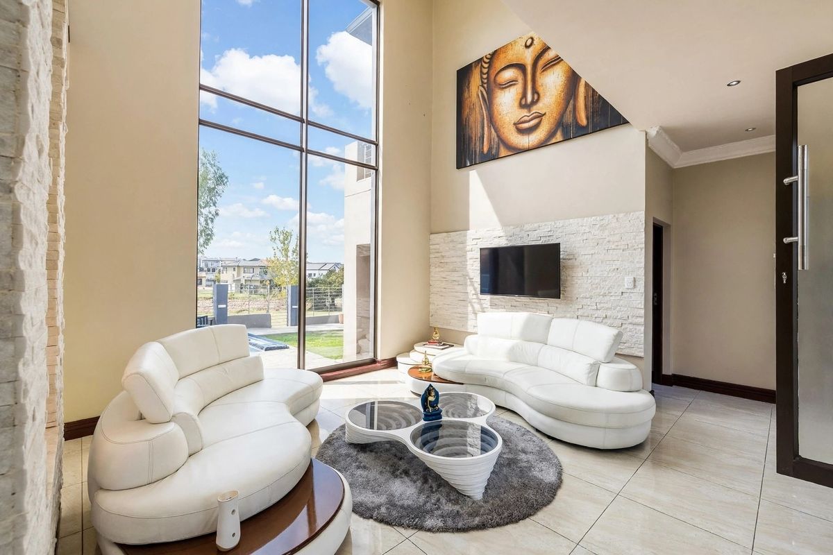 Spacious living room featuring double-volume windows, tiled flooring, and a striking stacked stone feature wall with integrated television mount.