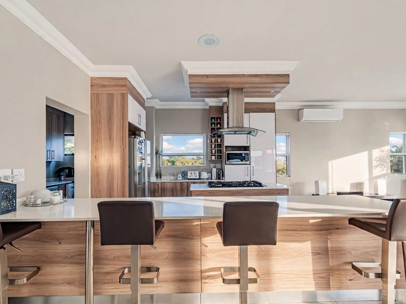 Modern kitchen featuring a large island with breakfast bar seating, high-end built-in appliances, stone countertops, and sleek wood-grain cabinetry.