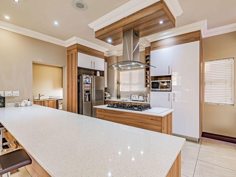 Modern kitchen featuring high-gloss cabinetry, quartz countertops, a central island with a gas hob, and integrated appliances with recessed lighting.