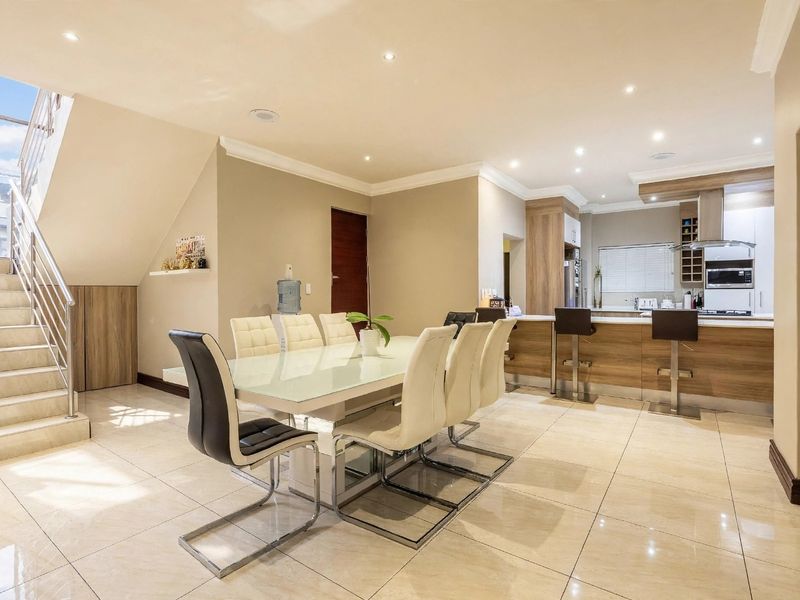 Spacious open-plan living and dining area featuring modern porcelain tiles, a sleek kitchen island, and a contemporary staircase with glass balustrades.