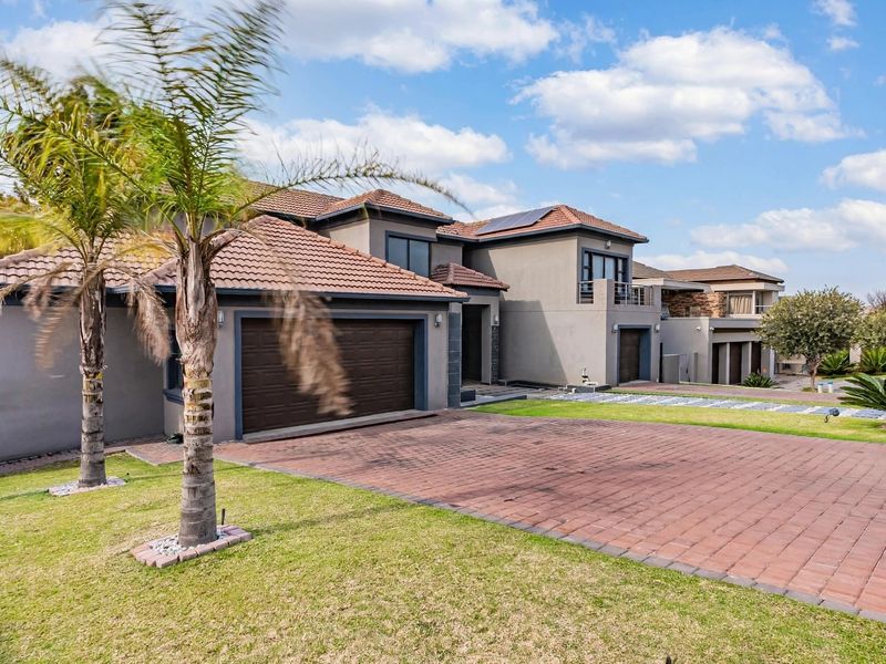 A modern double-story residential property featuring a paved driveway, double garage, tiled roof, and solar panels, set within a well-maintained landscaped garden.