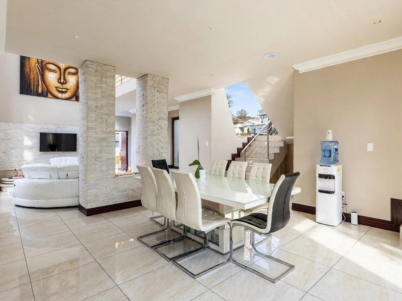 Spacious open-plan dining area featuring stone-clad columns, polished tiled flooring, and a modern staircase leading to the upper level.