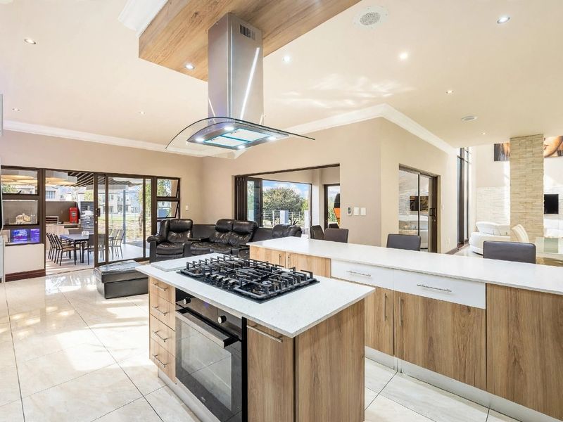 Modern open-plan kitchen featuring a central island with gas cooktop, stone countertops, and seamless flow to the outdoor patio area.