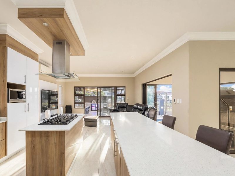 Modern open-plan kitchen and living area featuring a large island with gas hob, stone countertops, and seamless flow to the outdoor patio.