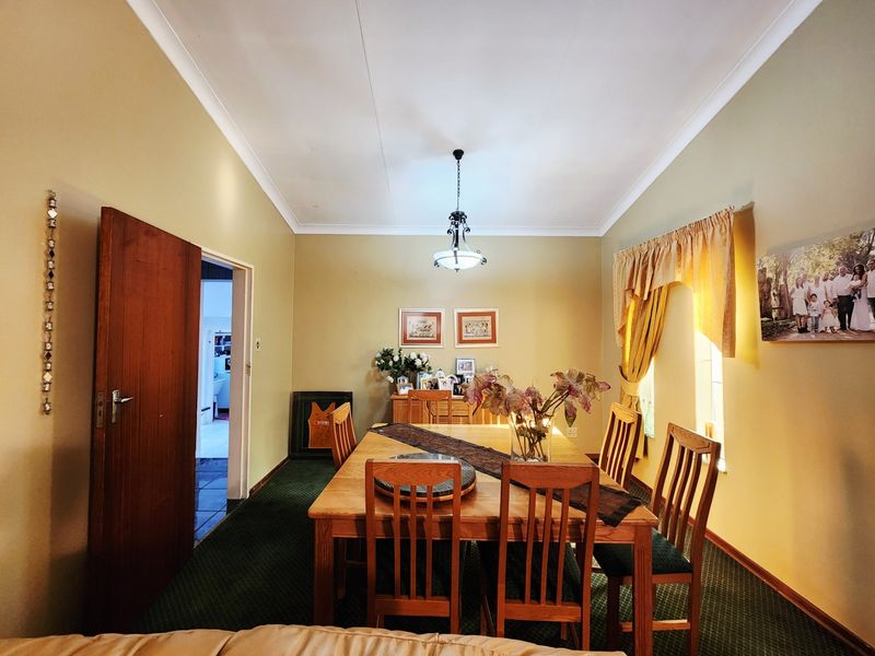 A traditional dining room featuring a central pendant light, cove cornicing, and a solid timber door leading to an adjacent space.
