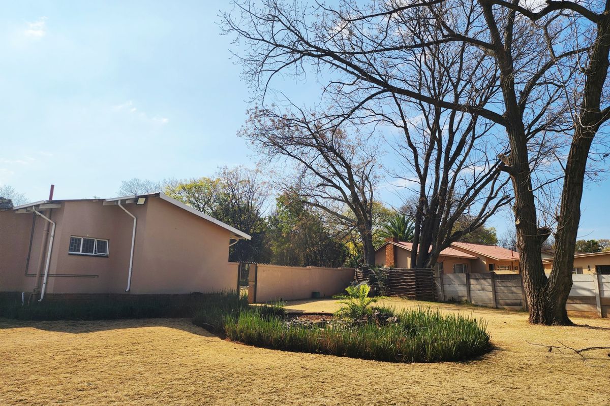 A view of the rear exterior of the house featuring a landscaped garden bed, boundary wall, and mature trees.