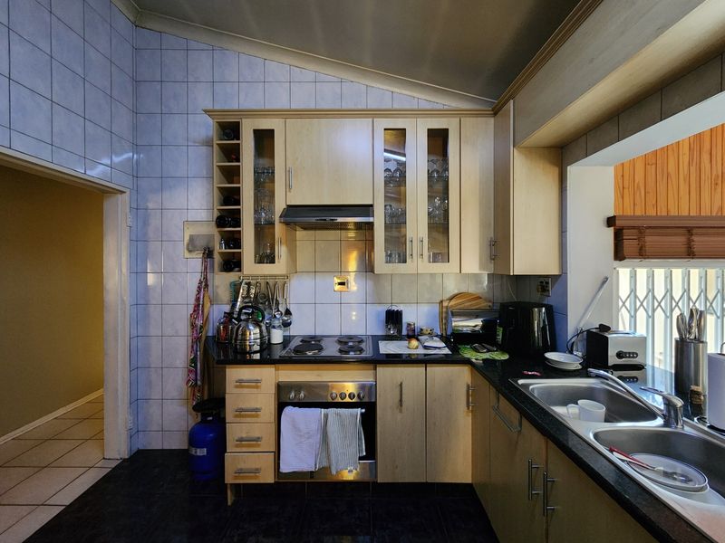 A functional kitchen featuring light wood cabinetry, a built-in oven and hob, extractor fan, and a double bowl sink with tiled splashbacks.