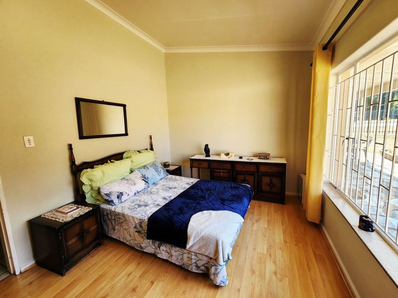A well-lit bedroom featuring laminate flooring, large windows with security bars, and neutral wall finishes.