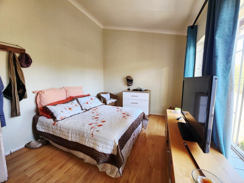 A functional bedroom featuring laminate flooring, neutral wall tones, and a sliding glass door providing natural light and access to the exterior.