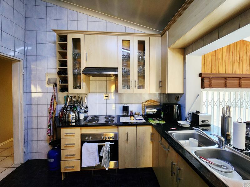 A functional kitchen featuring light wood cabinetry, granite countertops, a built-in oven with electric hob, and a double stainless steel sink.