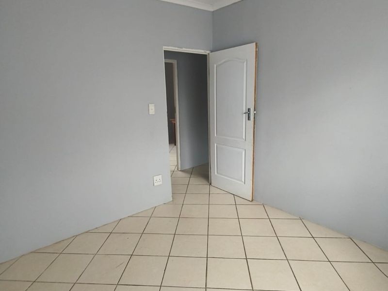 An empty bedroom featuring neutral grey walls, ceramic floor tiles, and a simple ceiling light fixture, ready for personalization.