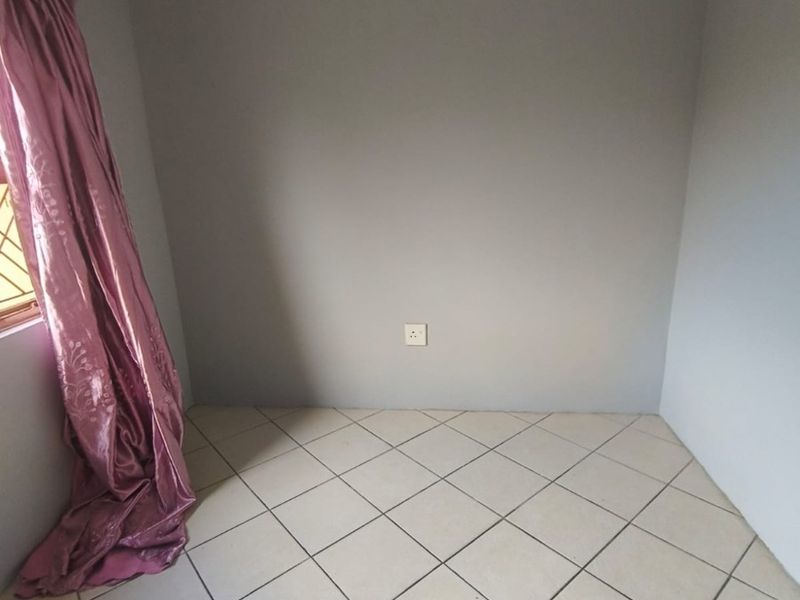 A vacant bedroom featuring neutral grey walls, tiled flooring, and a single electrical outlet, providing a blank canvas for personalization.
