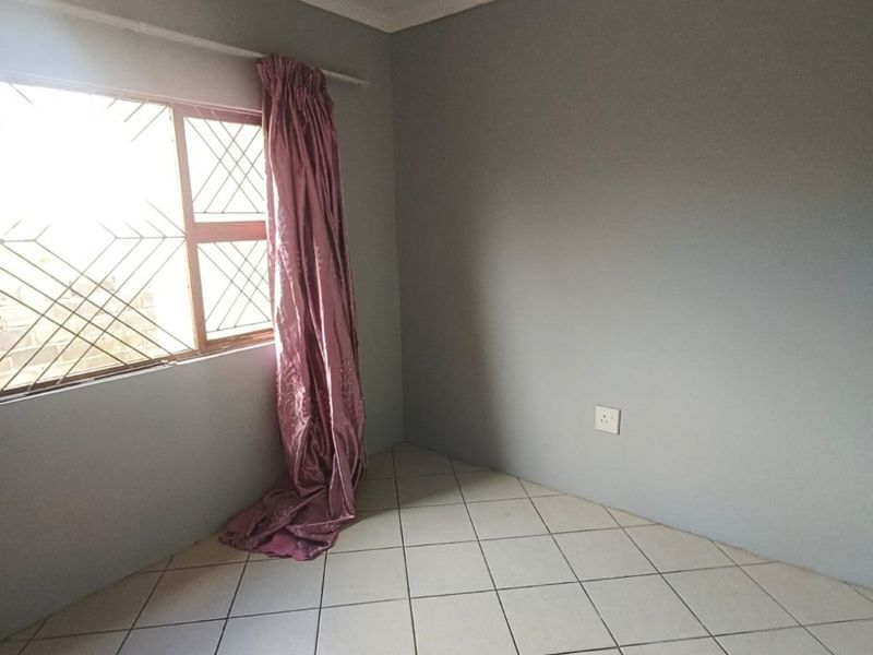 A vacant bedroom featuring neutral grey walls, tiled flooring, and a window fitted with security bars.