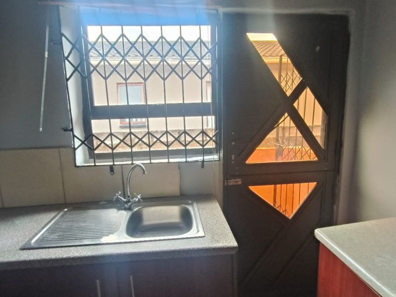 A functional kitchen area featuring built-in cabinetry, a stainless steel sink with mixer tap, tiled flooring, and a security gate leading to the exterior.