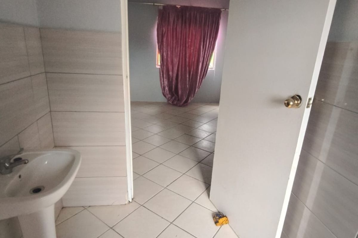 A functional bathroom featuring a pedestal sink, tiled walls, and tiled flooring, with an open doorway leading to an adjacent room.