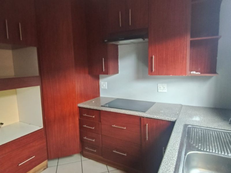 A functional kitchen featuring dark wood cabinetry, granite countertops, a built-in electric hob with extractor fan, and tiled flooring.